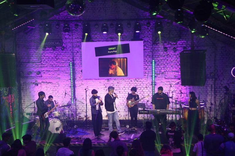 A full band on stage under purple light and green lasers