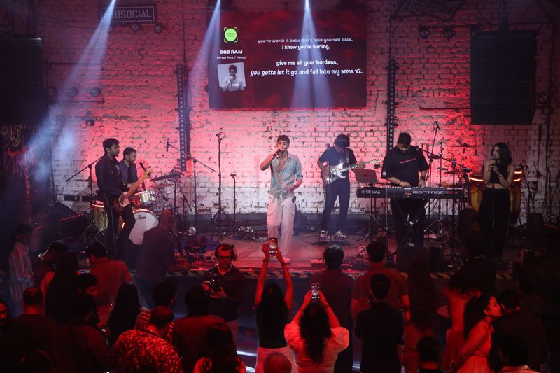 A band on a red-lit stage, phones raised in the front row