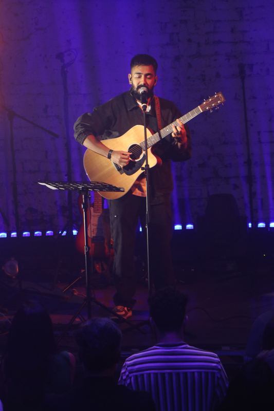 A singer with an acoustic guitar alone on a purple-lit stage